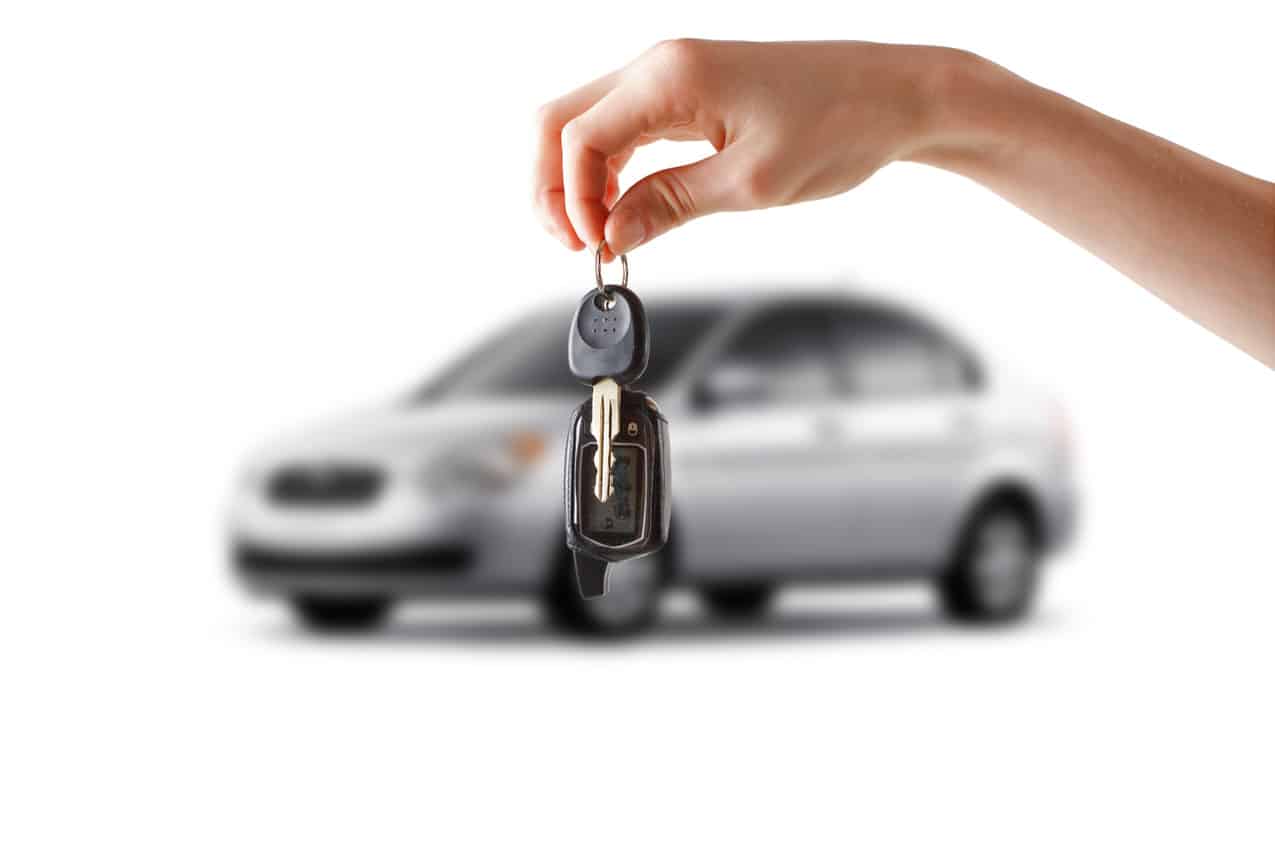 Mão segurando chaves de carro e um veículo desfocado ao fundo