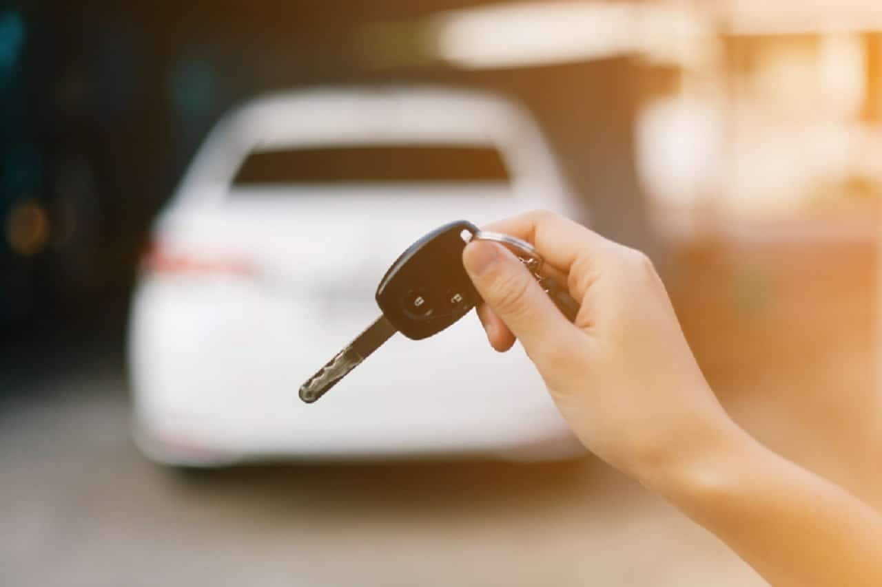 Imagem de uma pessoa segurando uma chave e apontando para um carro desfocado.