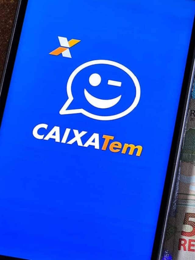 Celular com a logo do Caixa Tem na tela, em cima de várias notas de R$ 50 e R$ 100.