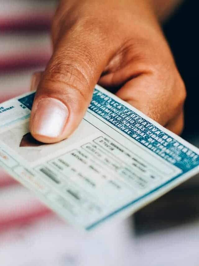 Mão entregando CNH. Fundo desfocado.