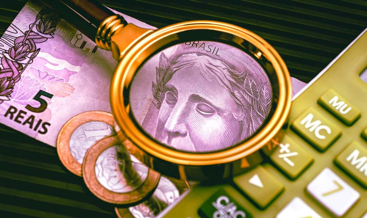 Lupa colocada apoiada sobre calculadora e sobre nota de cinco reais e moedas