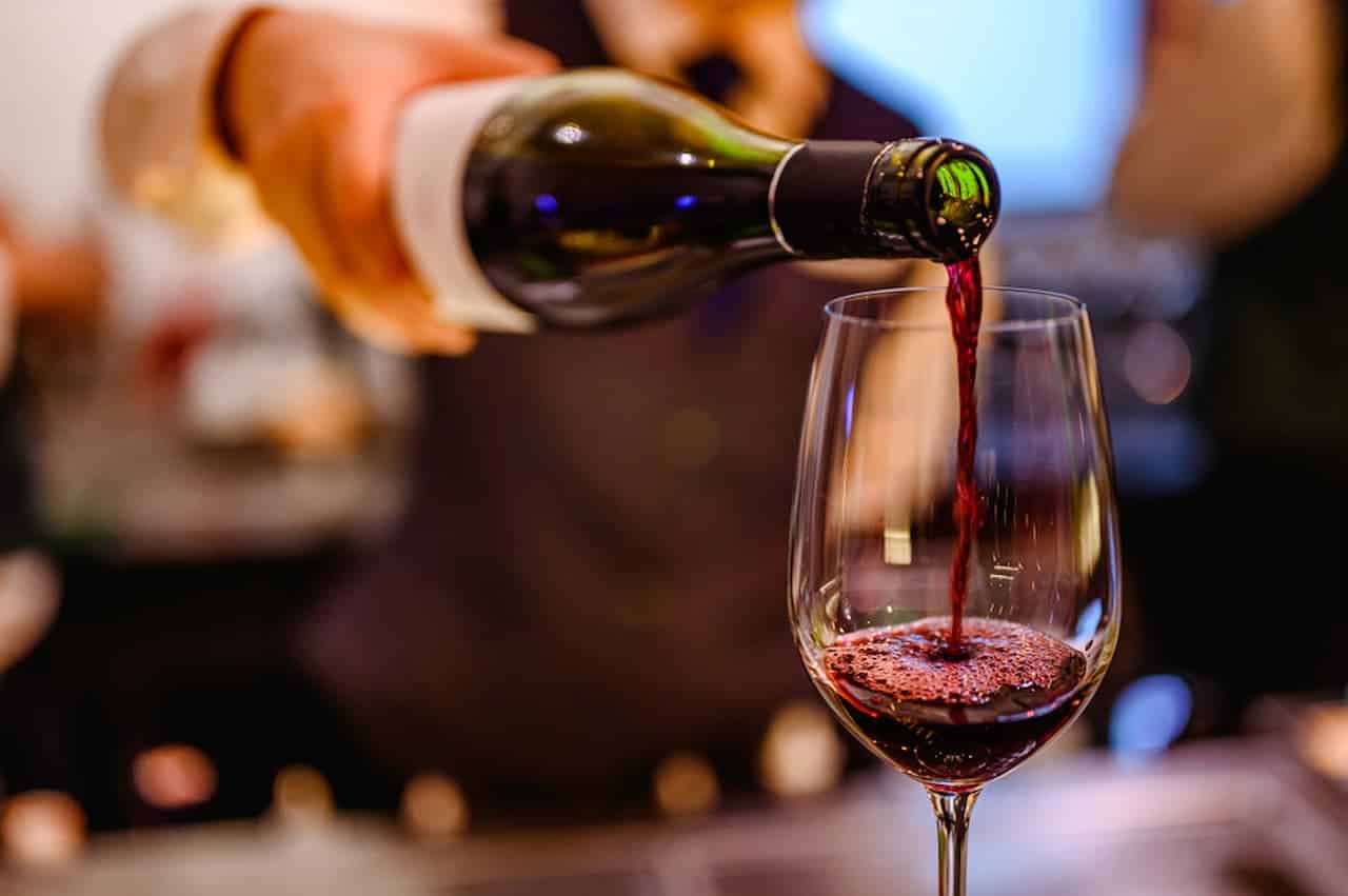 Pessoa segurando uma garrafa de vinho e servindo taça