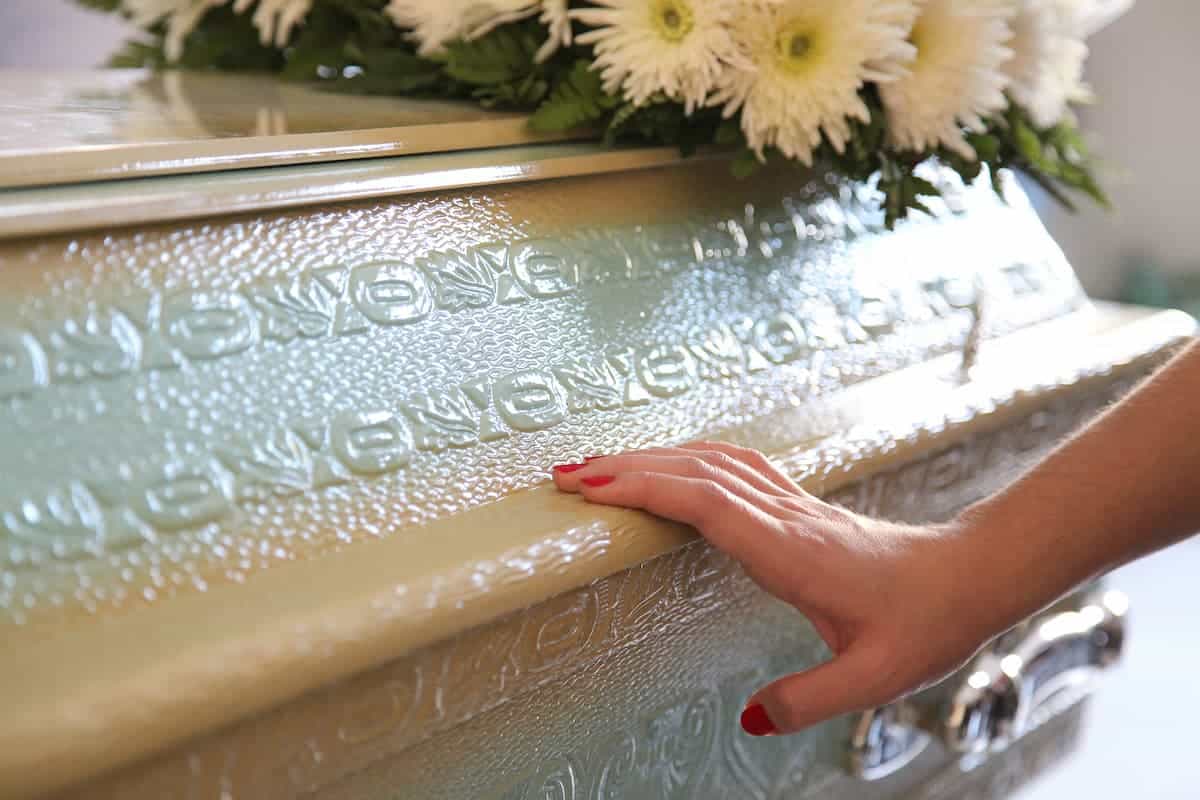 Imagem de mão encostada em um caixão branco.