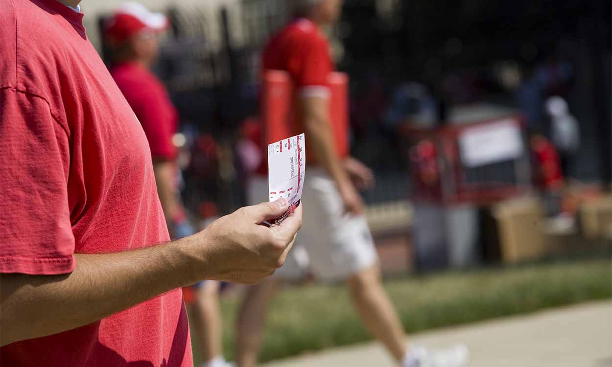 Imagem de um vendedor com camisa vermelha segurando um ingresso de evento.
