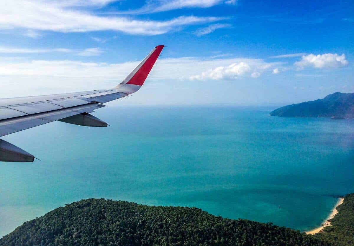 Imagem da asa de um avião sobrevoando uma ilha na Malásia