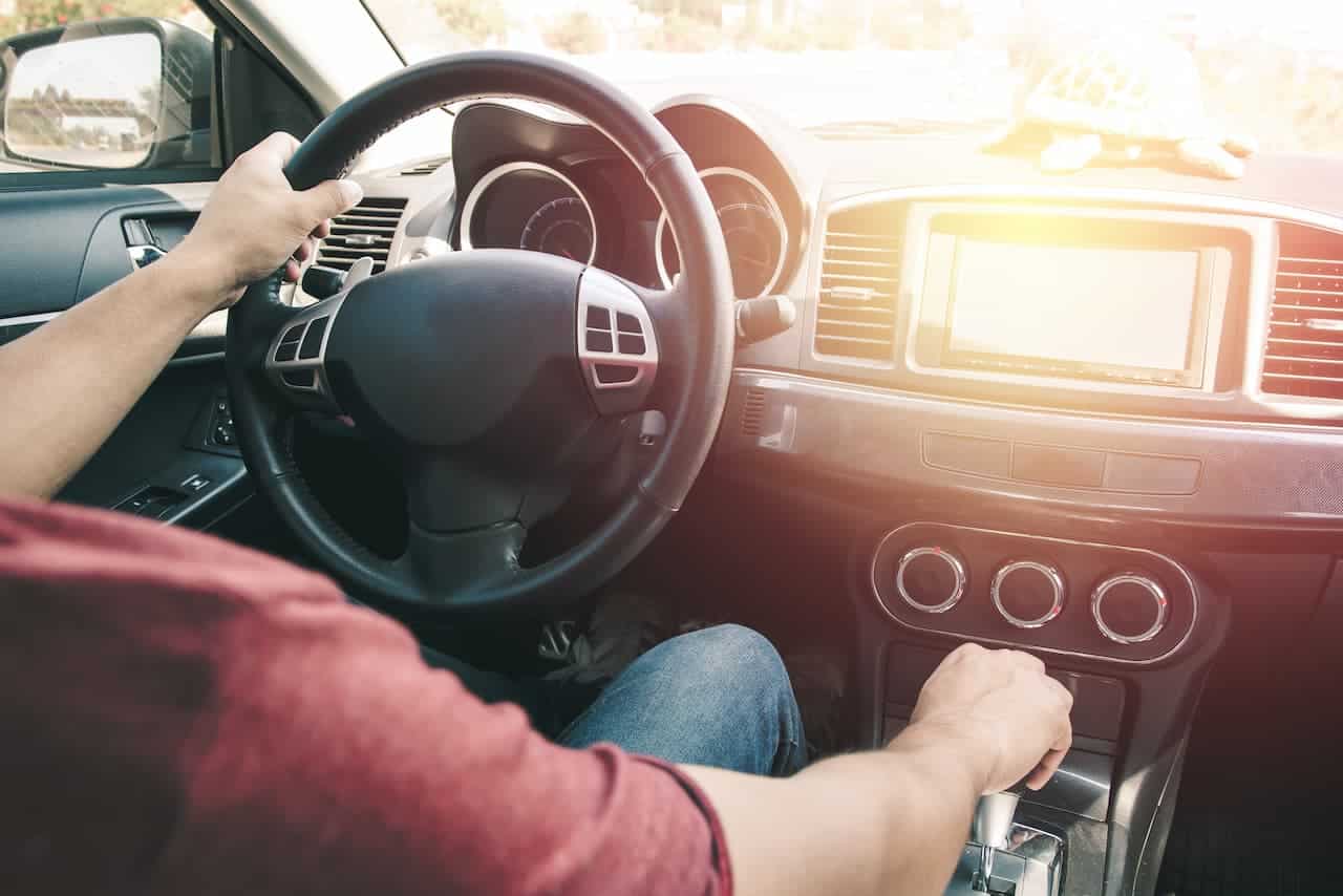 Motorista dentro de carro. seu rosto não aparece, uma mão está no volante e outra no câmbio.