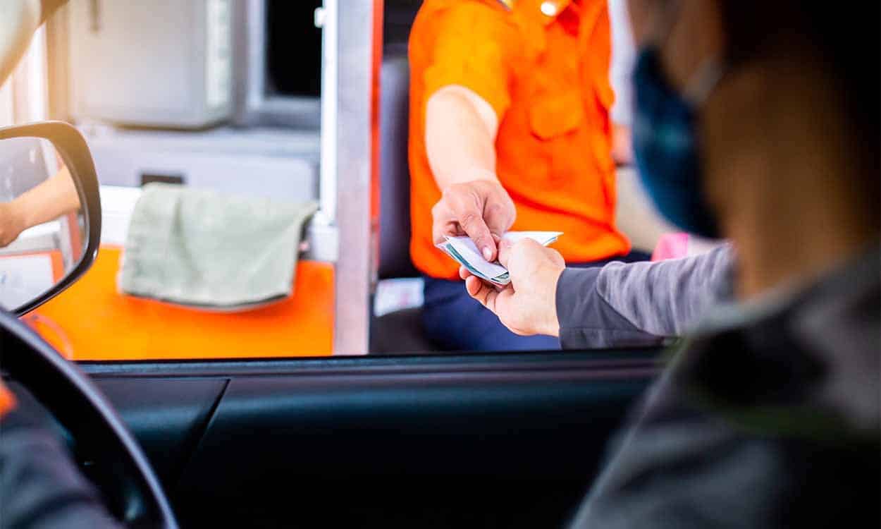 Imagem de um motorista pagando um pedágio, visão de dentro do carro
