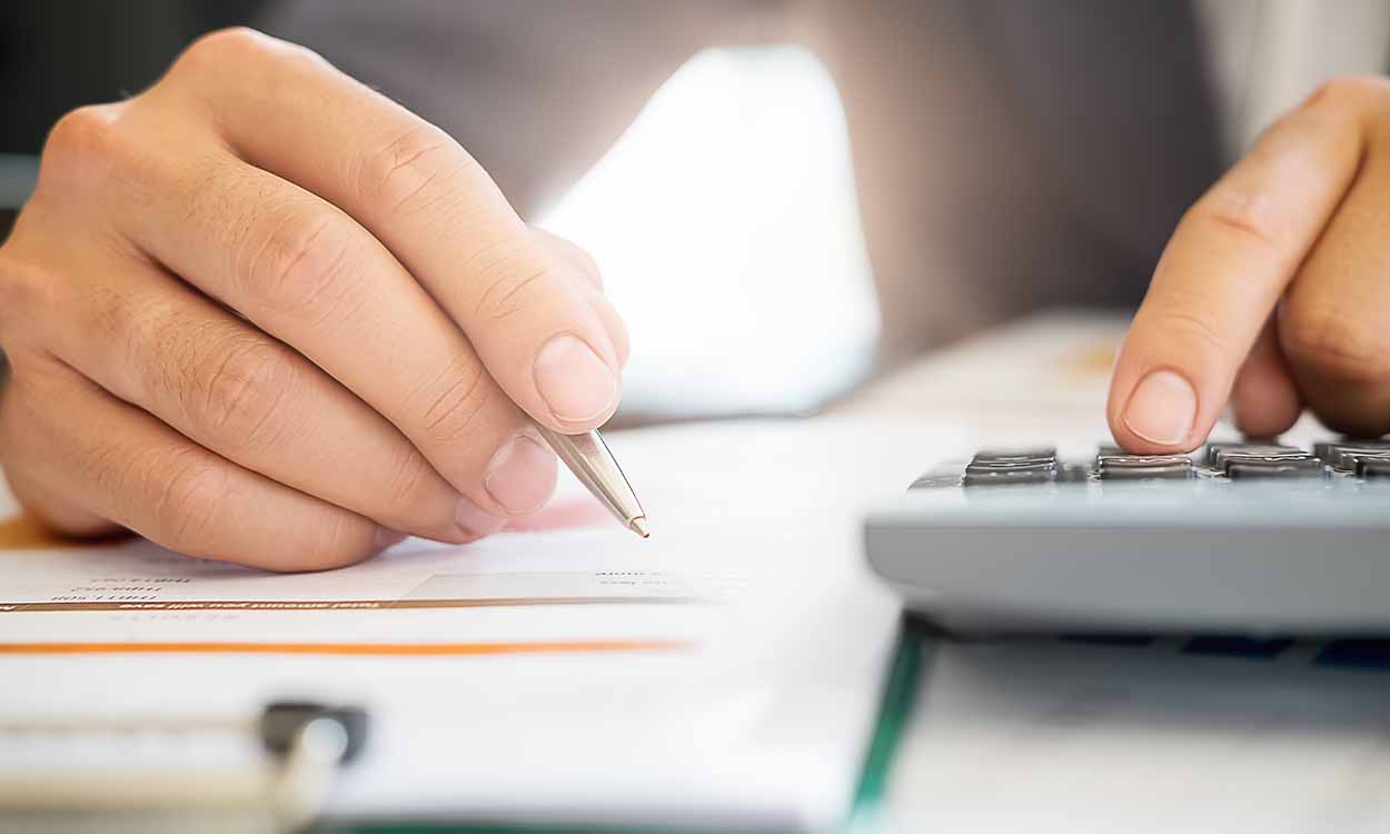 Imagem de uma pessoa utilizando uma calculadora e escrevendo