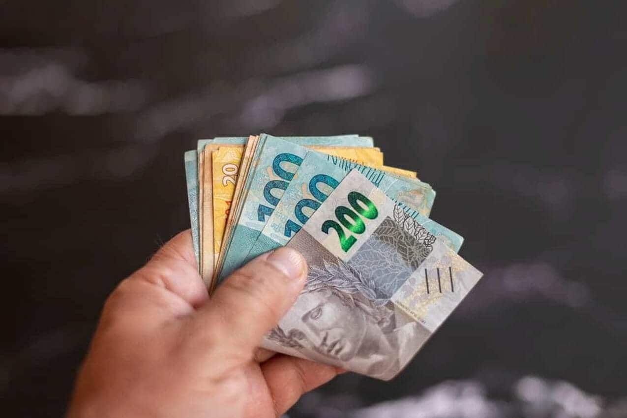 Mão segurando diversas notas de dinheiro dobradas.