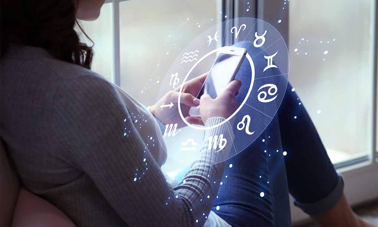 Pessoa mexendo no celular com desenho gráfico dos signos do zodiaco