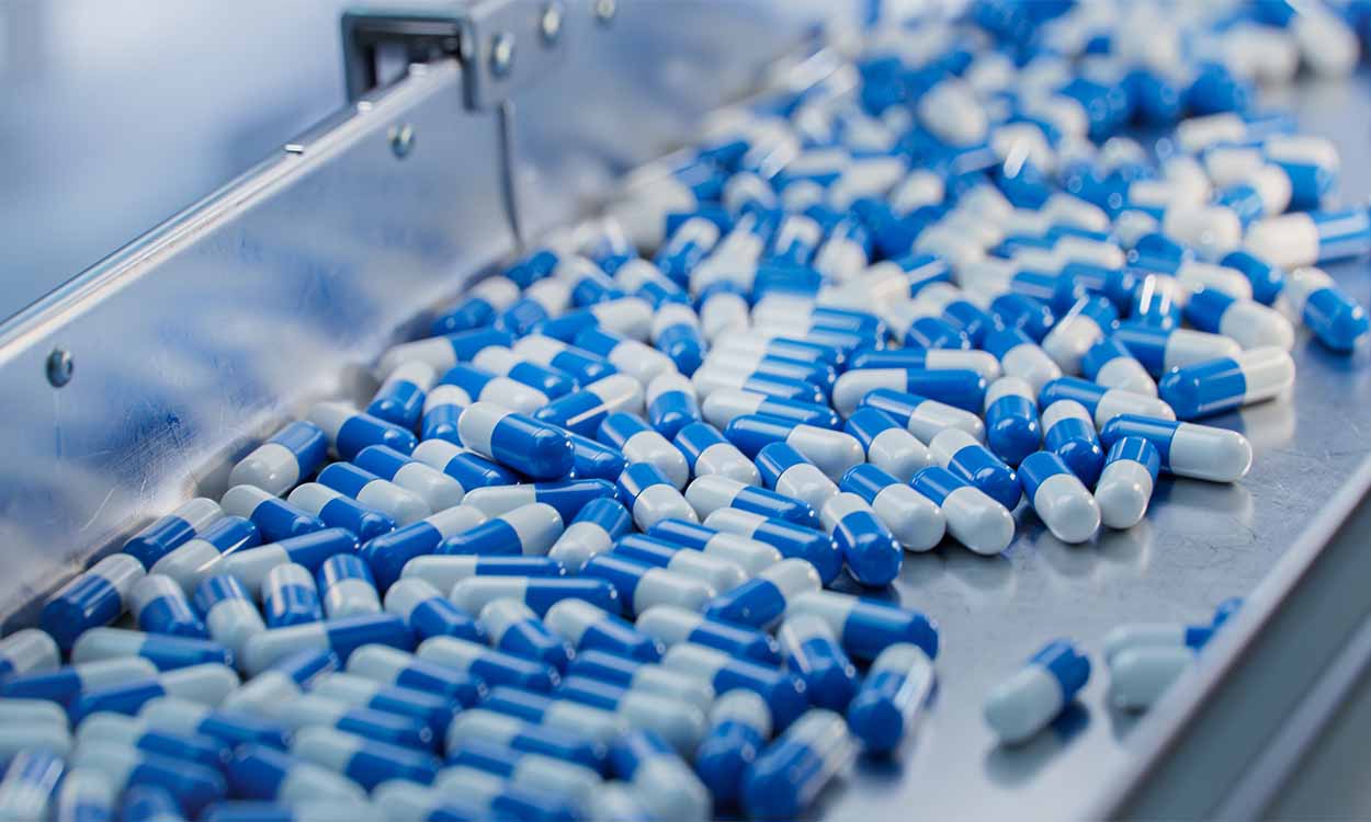 Várias pílulas de medicamentos nas cores azul e branco espalhadas em uma esteira.
