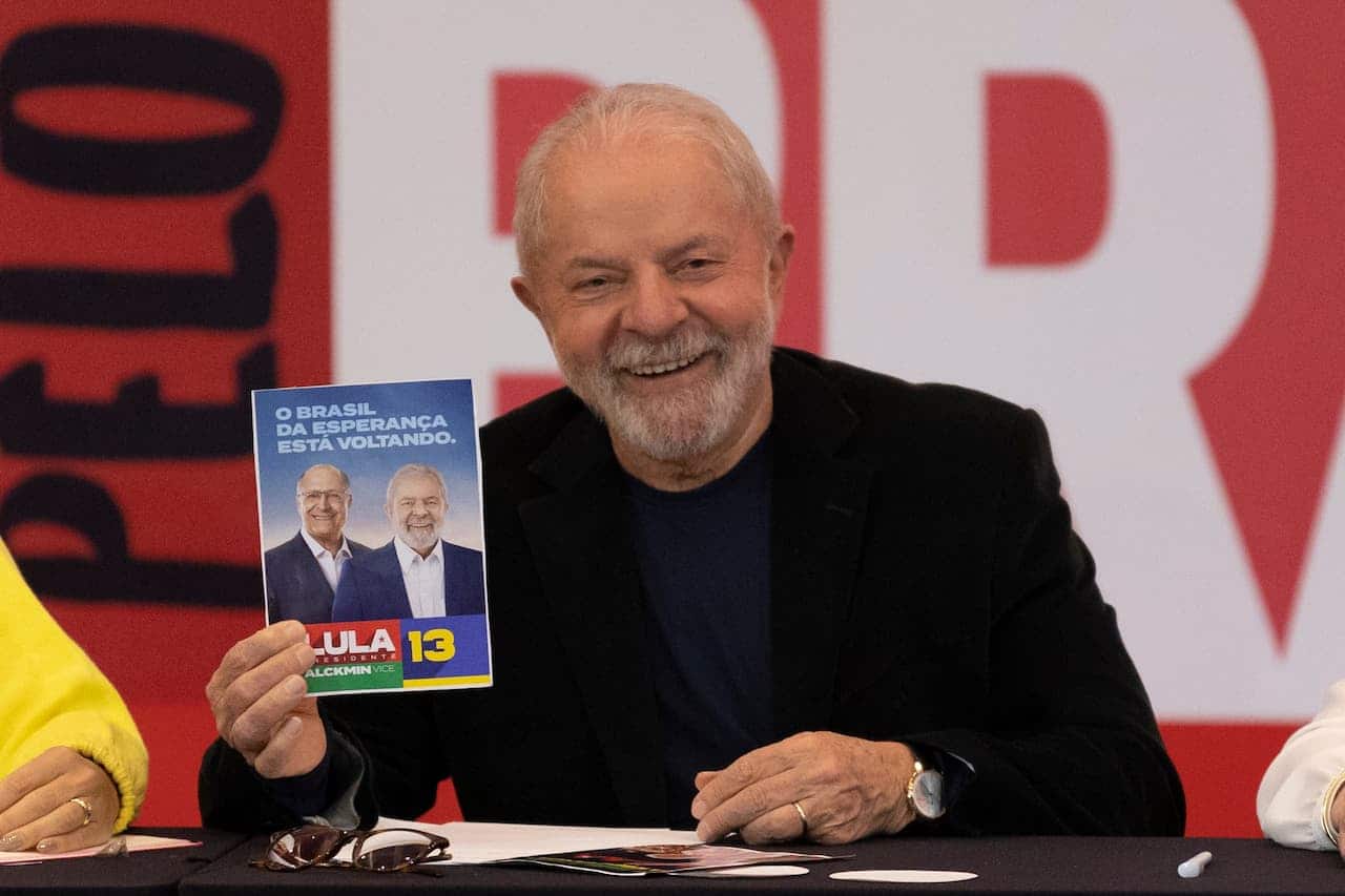presidente Luiz Inácio Lula da Silva segurando um folheto de campanha eleitoral e sorrindo com expressão de felicidade