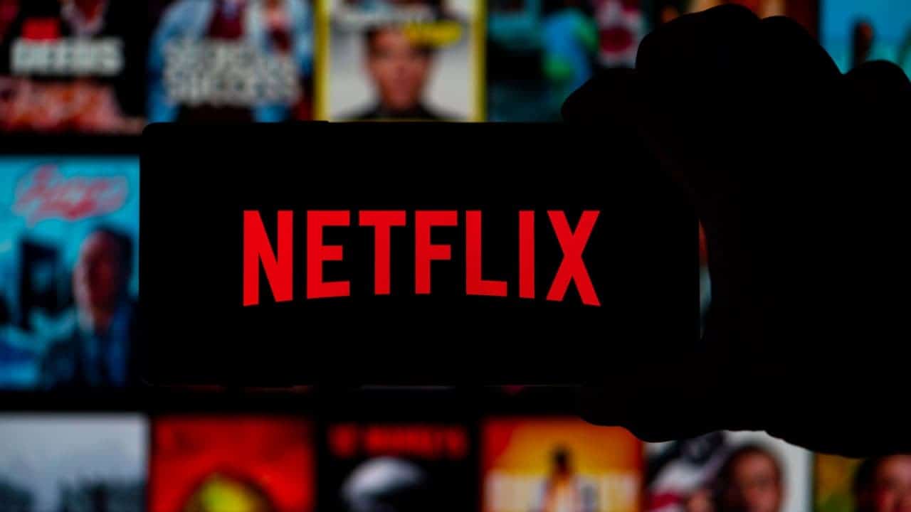 Imagem escurecida de uma pessoa segurando seu celular com o app da Netflix aberto em frente ao catálogo do streaming