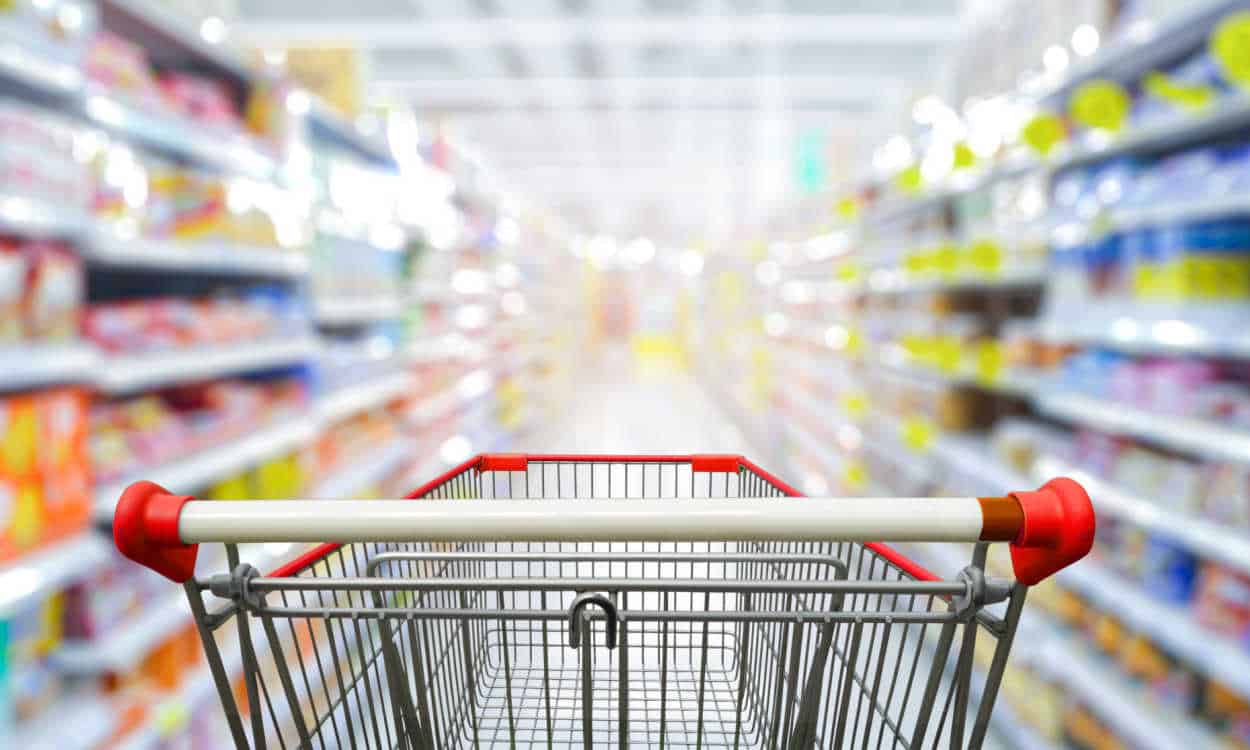 Imagem de um corredor de supermercado com o foco em um carrinho de compras