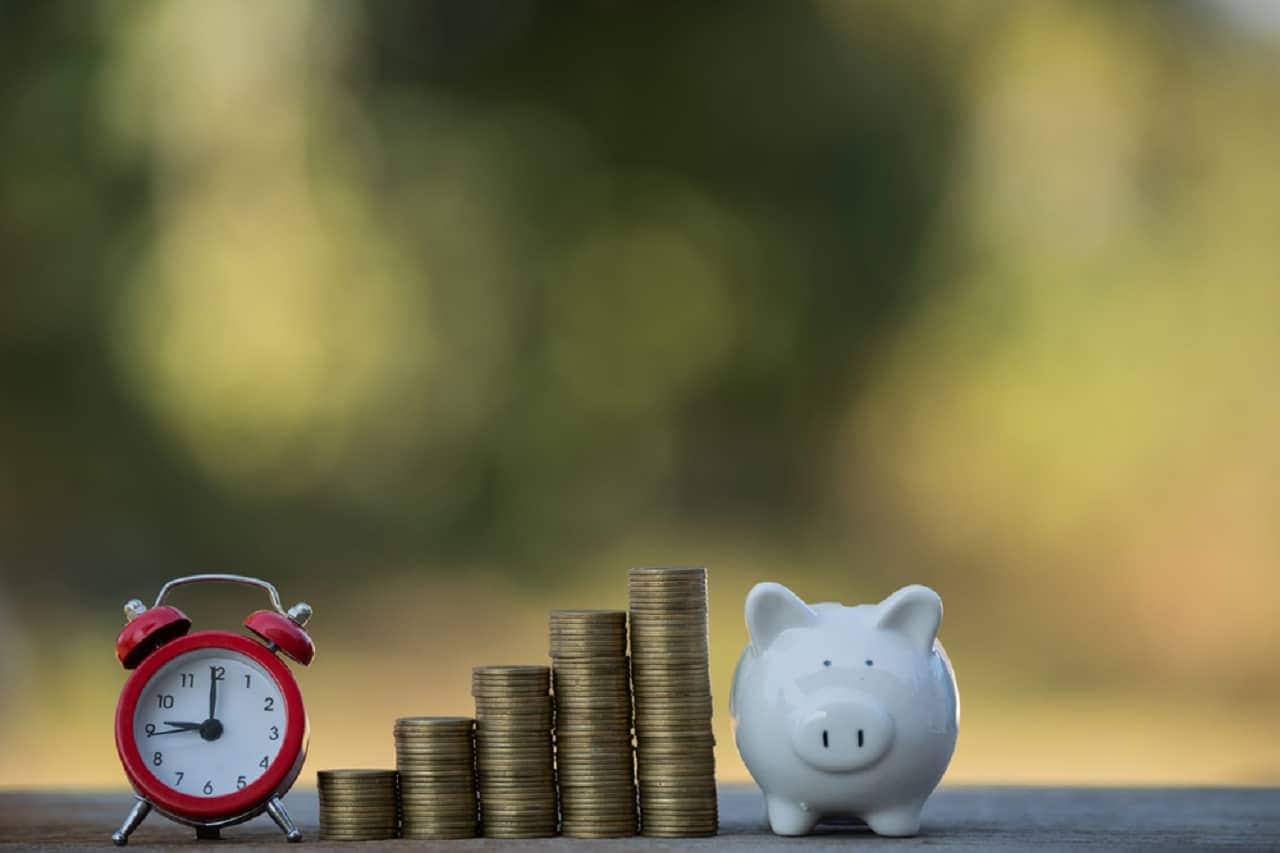 Imagem de um cofre, um relógio e pilhas de moedas.