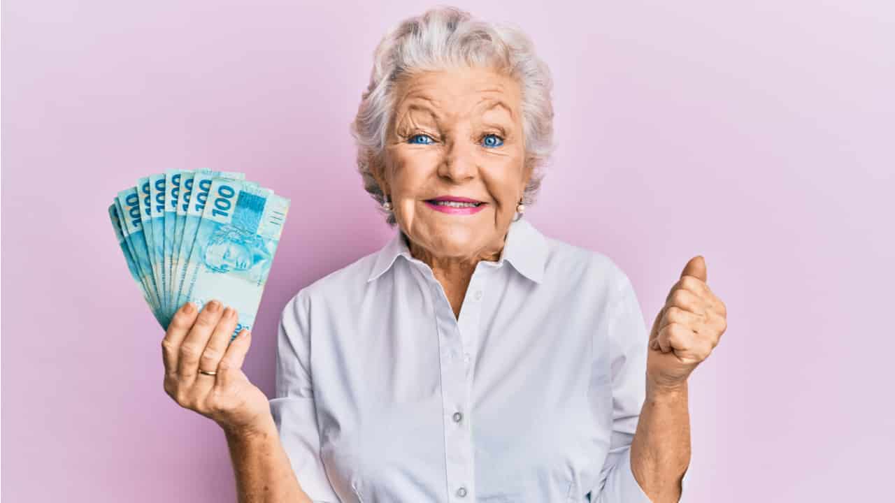Idosa aposentada com notas de 100 reais na mão enquanto sorri