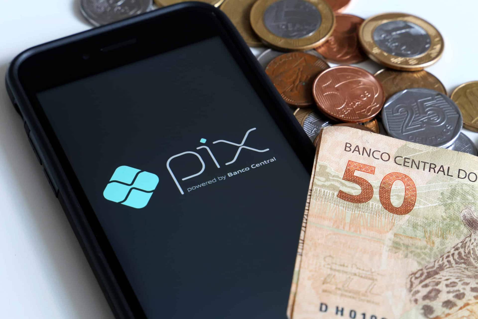Pix aberto no celular ao lado de nota de R$50,00 e algumas moedas