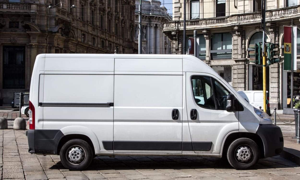 Imagem da lateral de uma van branca, que está em um local que parece uma praça pública