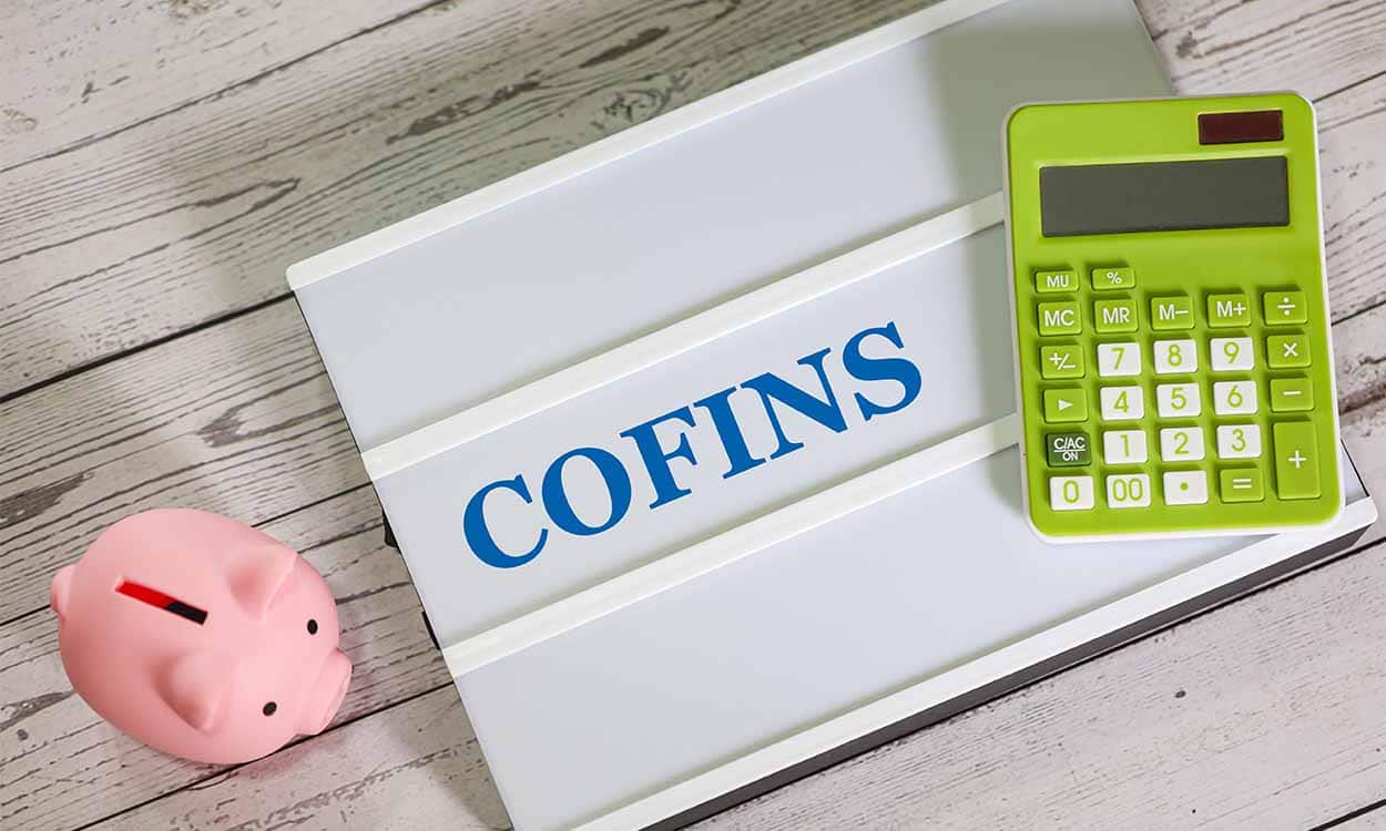Cofre em formato de porco e calculadora próxima da placa em que está escrito Cofins