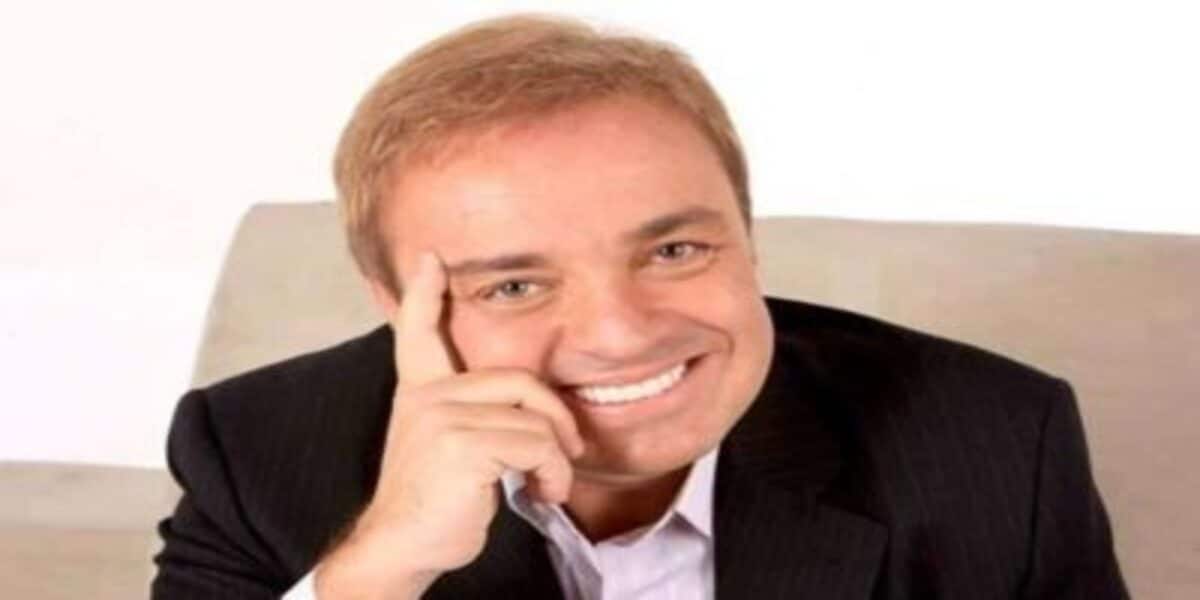Apresentador de TV, Gugu Liberato, sorrindo e com a mão no rosto