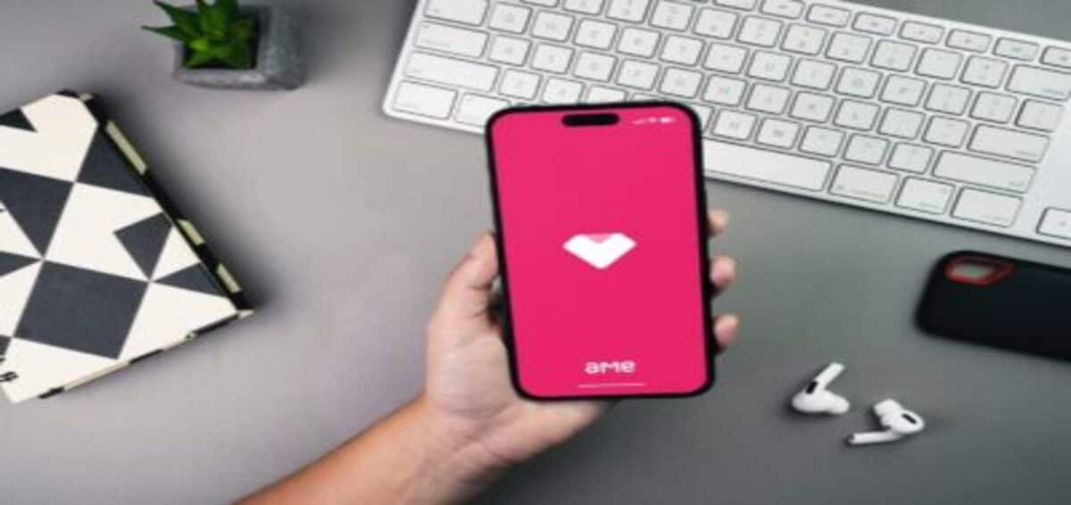 pessoa segurando celular com aplicativo ame digital, ao fundo tem um teclado branco de computador