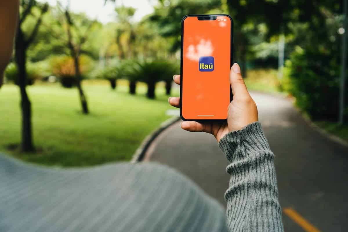 Aplicativo Itaú em celular de cliente com rua e praça ao fundo