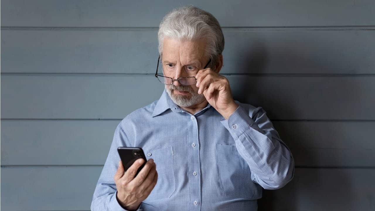 Homem idoso olhando para o celular com cara de assombro