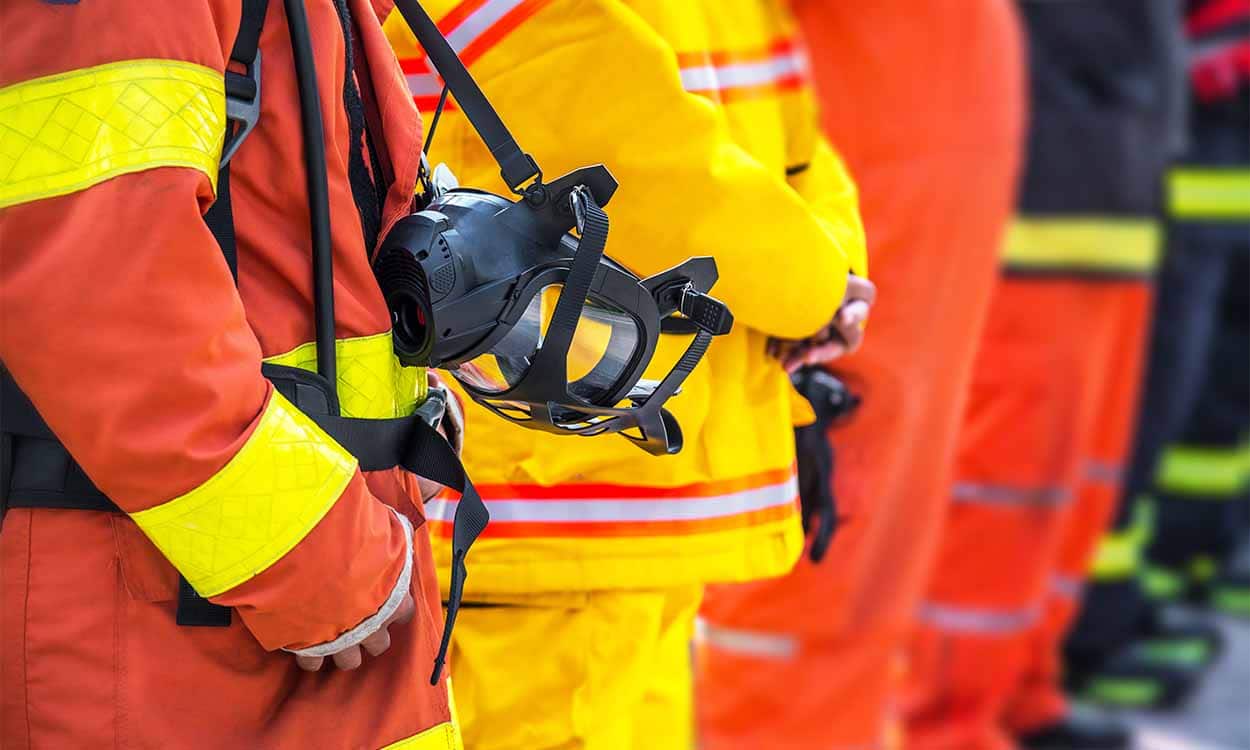 Bombeiros enfileirados. A imagem foca apenas da cabeça pra baixo, em seus uniformes.
