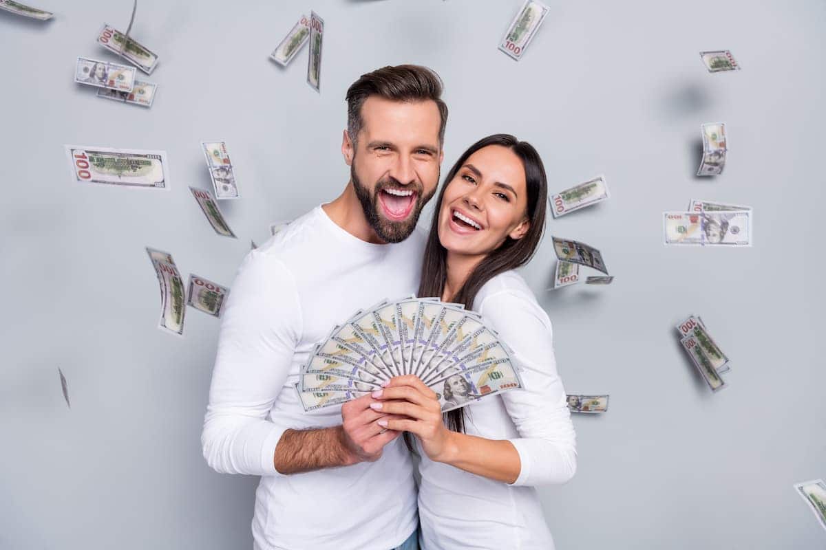 Casal segurando grande quantidade de dinheiro enquanto notas caem ao fundo