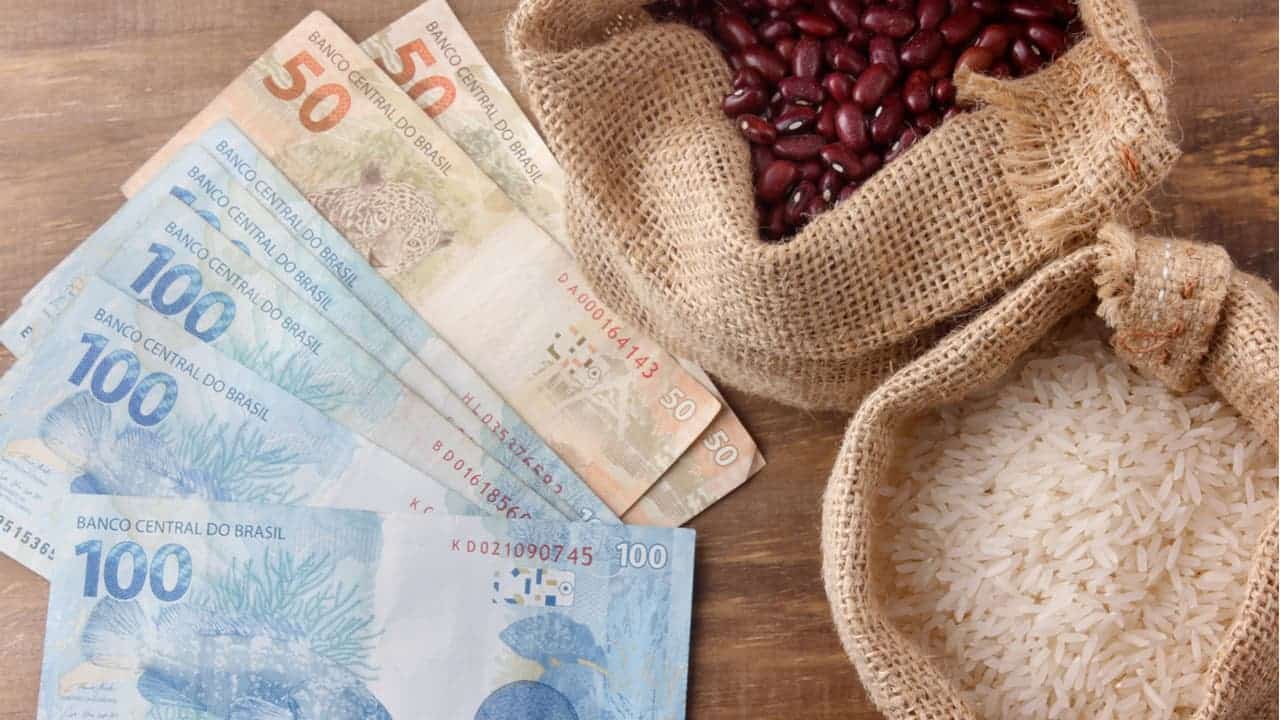 Notas de 100 e 50 reais ao lado de sacos de feijão e arroz