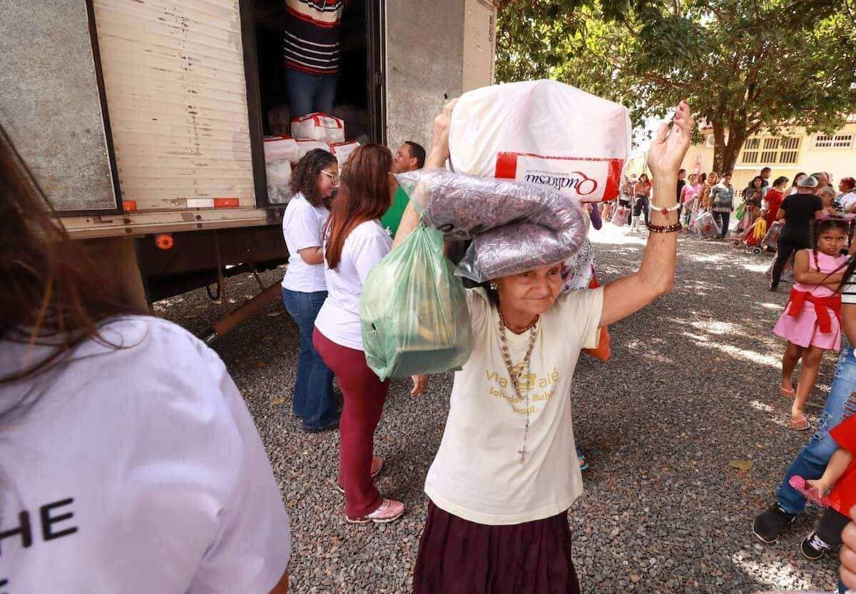 Na imagem, idosa carrega uma cesta básica nas costas.