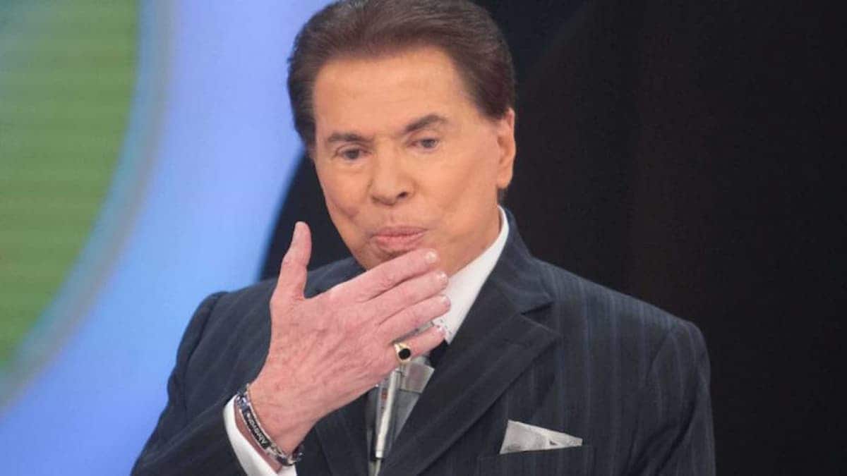 Imagem do apresentador Silvio Santos com as mãos no rosto.