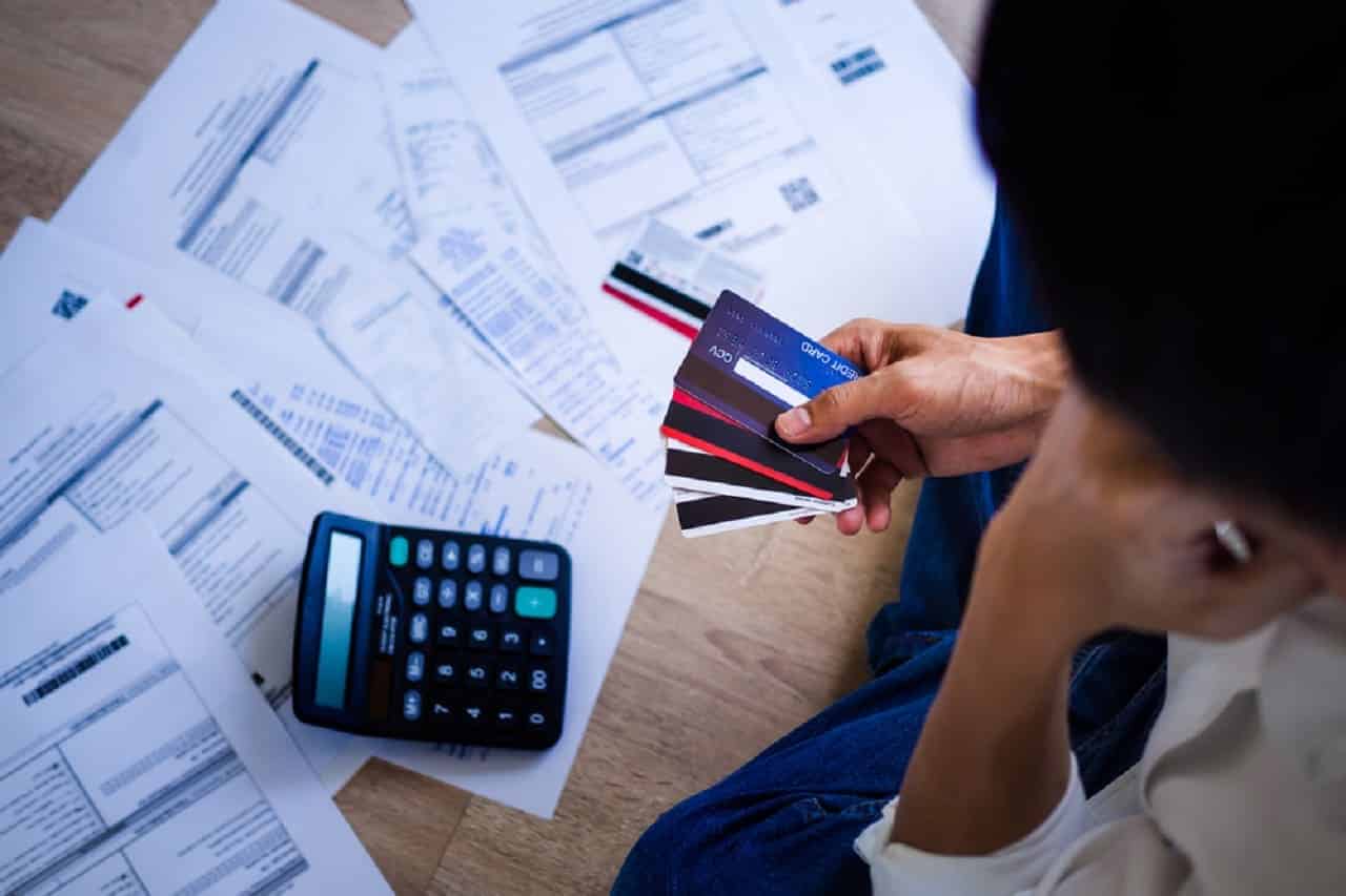 Imagem de uma pessoa segurando cartões e olhado para boletos e uma calculadora