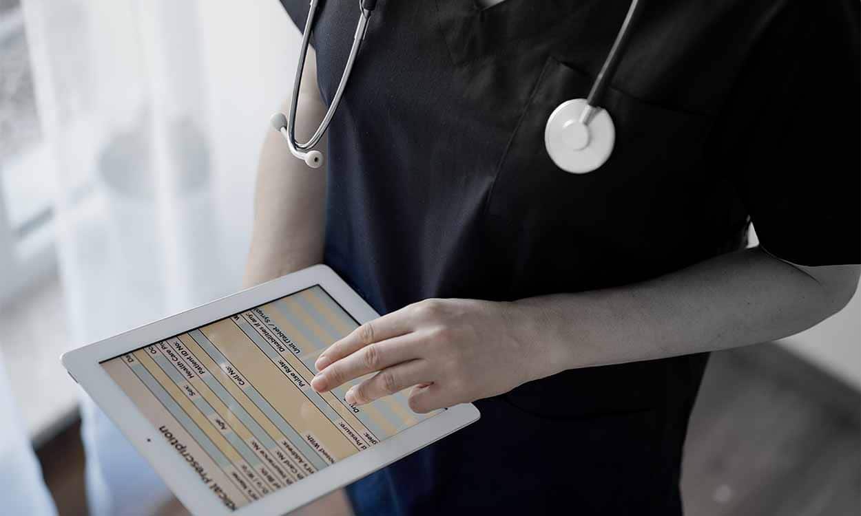 Pessoa com estetoscópio no pescoço enquanto segura tablet com ficha digital