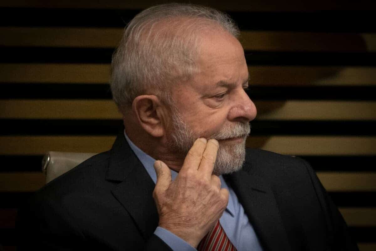 Presidente Lula sentado, com o rosto virado de lado e dois dedos tocando a face.