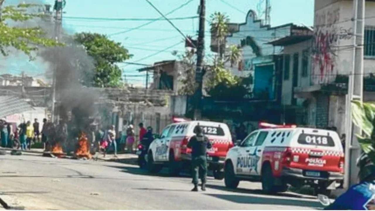 Policiais se aproximam de manifestantes que fecham avenida em Belém (PA). Ao fundo, é possível ver destroços pegando fogo e muita fumaça.