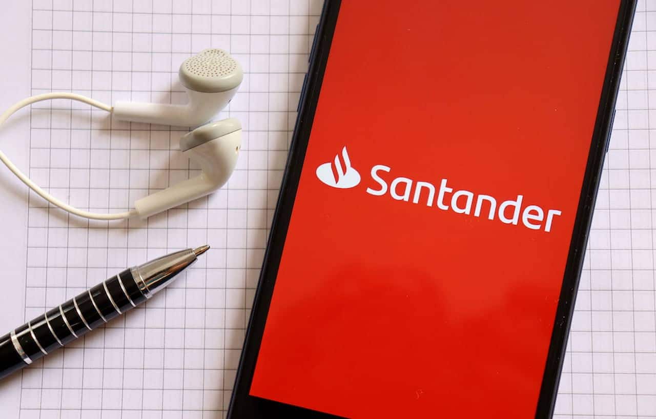 Ao lado de fones de ouvido e uma caneta, celular exibe tela inicial do app do Santander