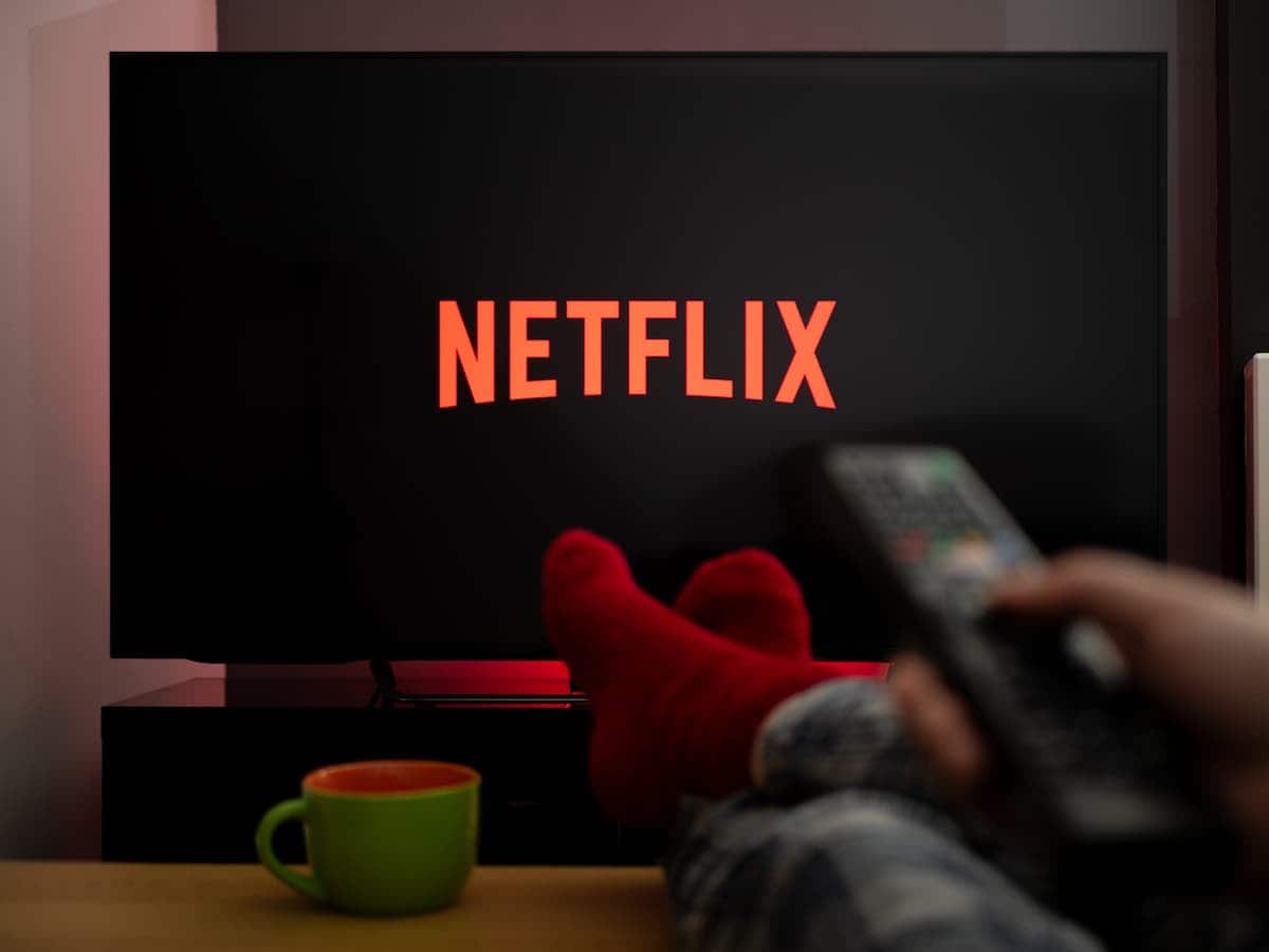 Usuário acessando Netflix através da televisão com pés apoiados sobre a mesa e sua mão segurando controle