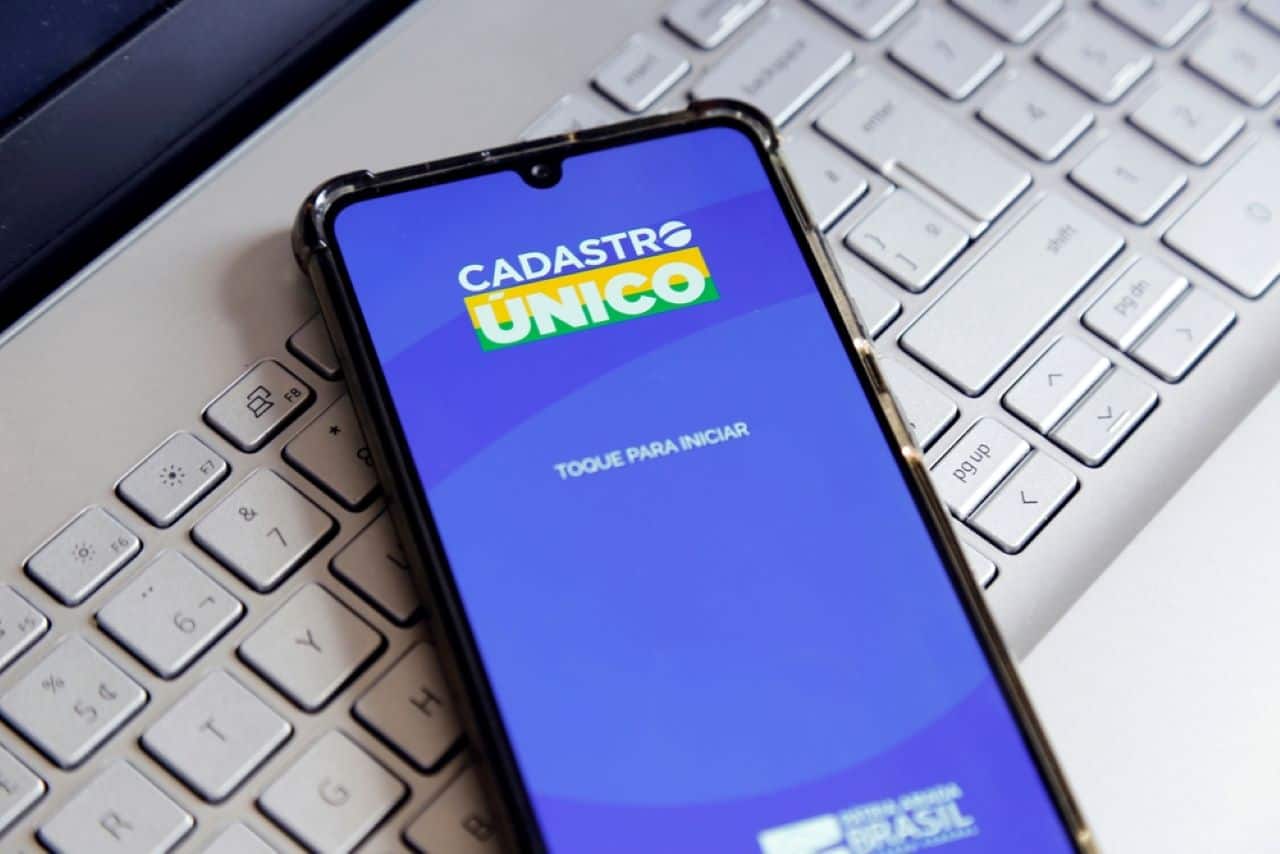 Na imagem, celular sobre teclado branco, exibindo app do CadÚnico na tela