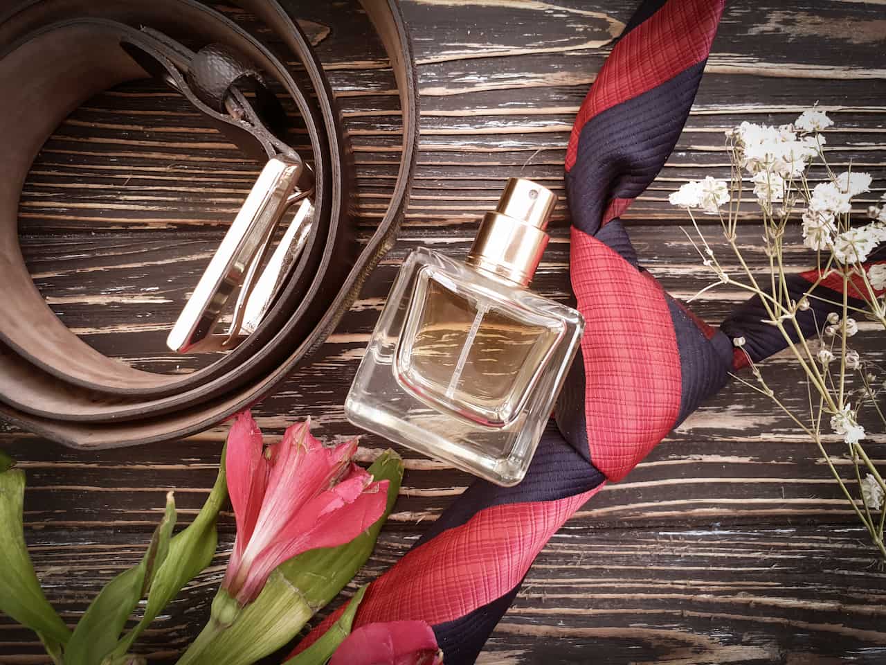 frasco de perfume quadrado, gravata vermelha e preta e um cinto marrom
