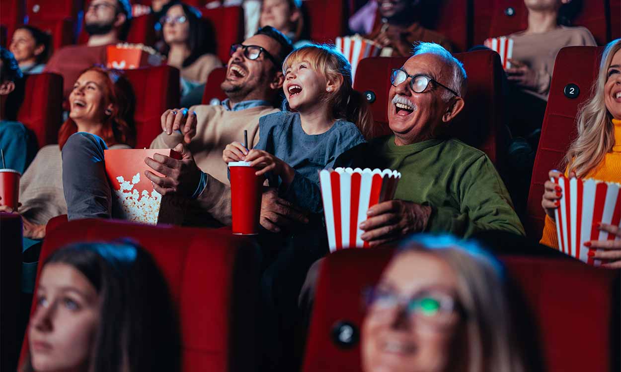 Pessoas sentadas numa sala de cinema, com expressões de felicidade, segurando pipocas