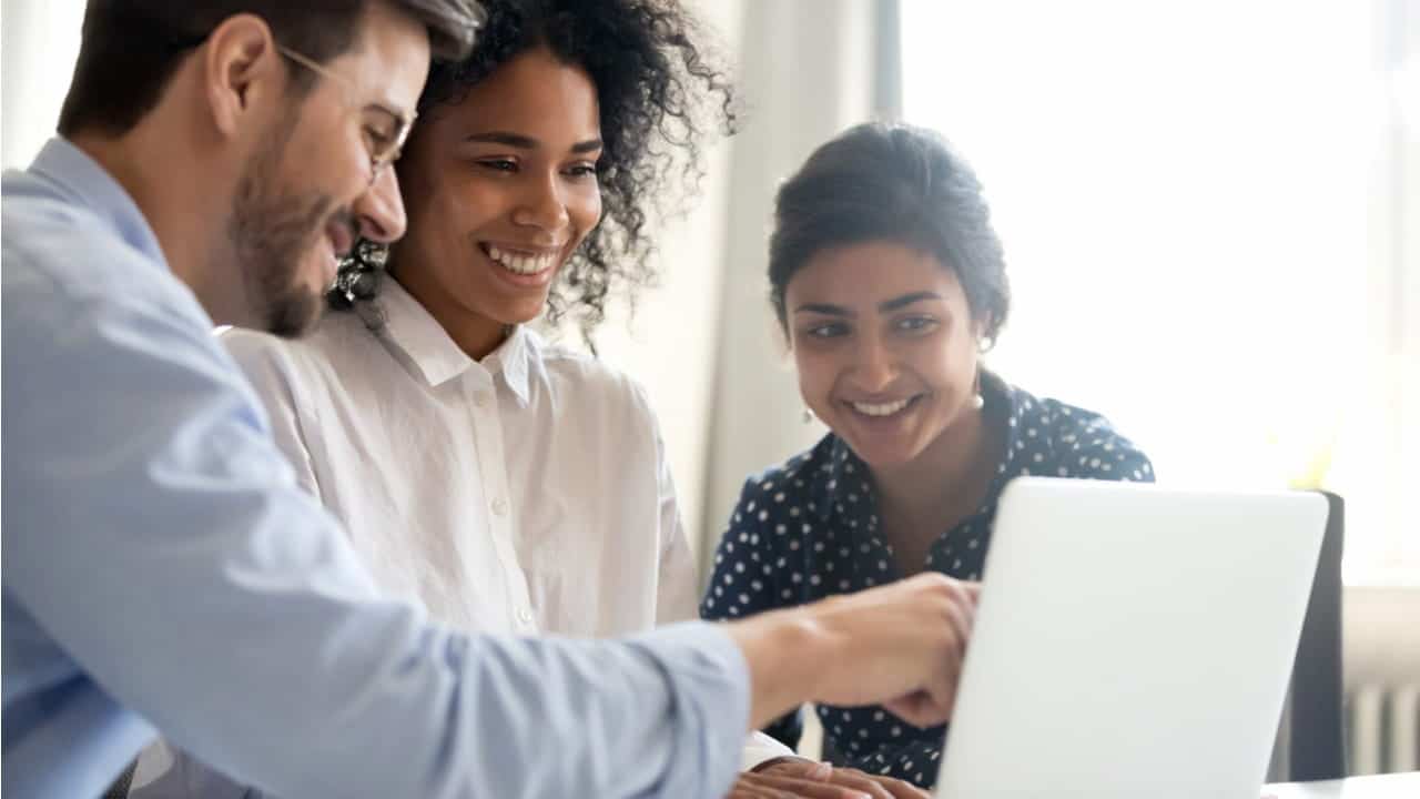 Três pessoas, um homem e duas mulheres, olhando a tela de um notebook e sorrindo