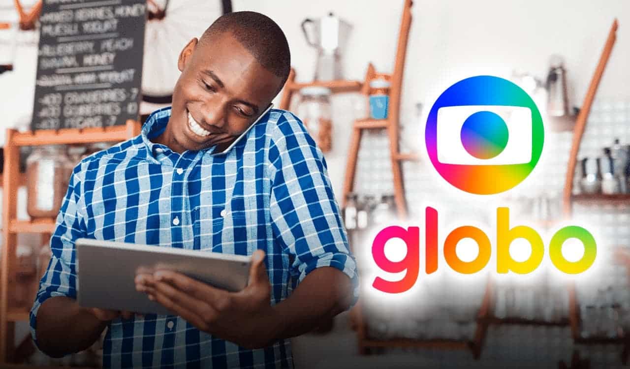 Homem sorridente falando no celular enquanto utiliza um tablet. Ao lado, aparece o logo da Rede Globo.