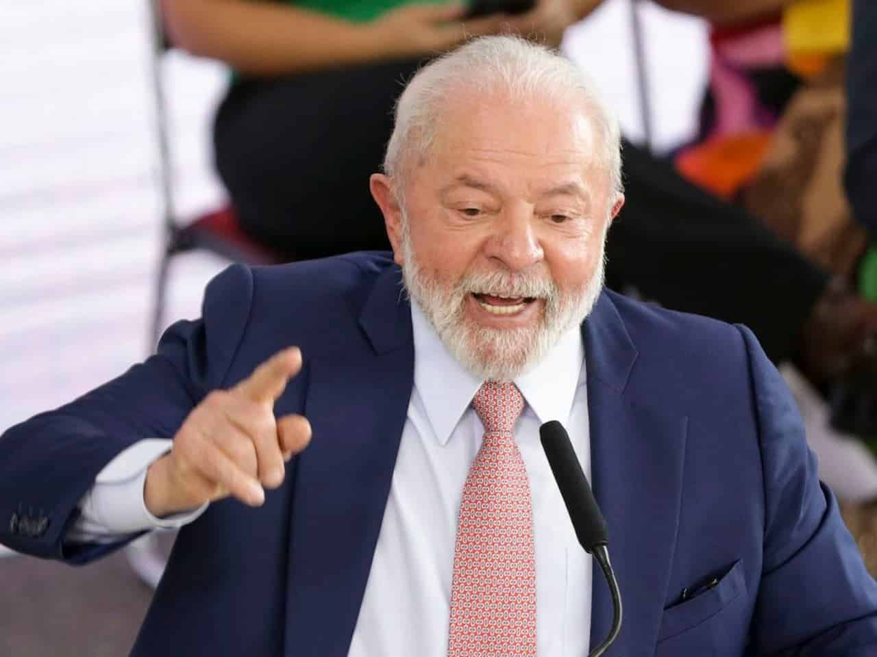 Presidente Lula vestido de terno azul e gravata rosa durante discurso com microfone à frente.