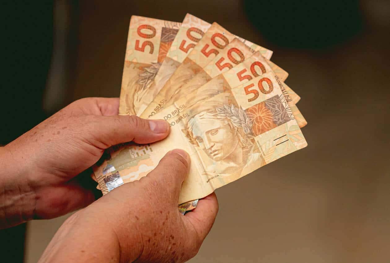 Pessoa segurando notas de cinquenta reais.
