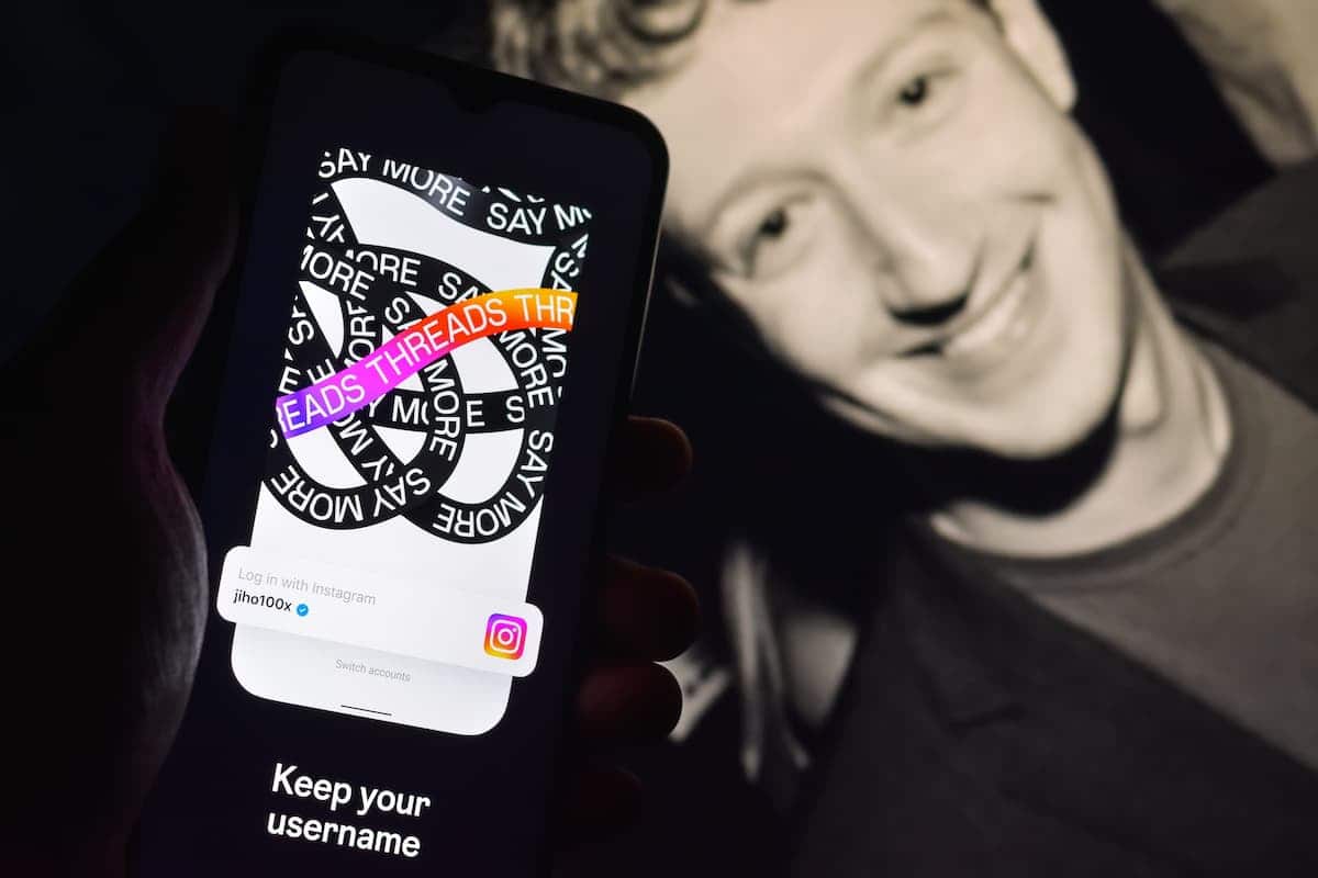 Mark Zuckerberg ao fundo com pessoa segurando celular enquanto usa plataforma do Threads