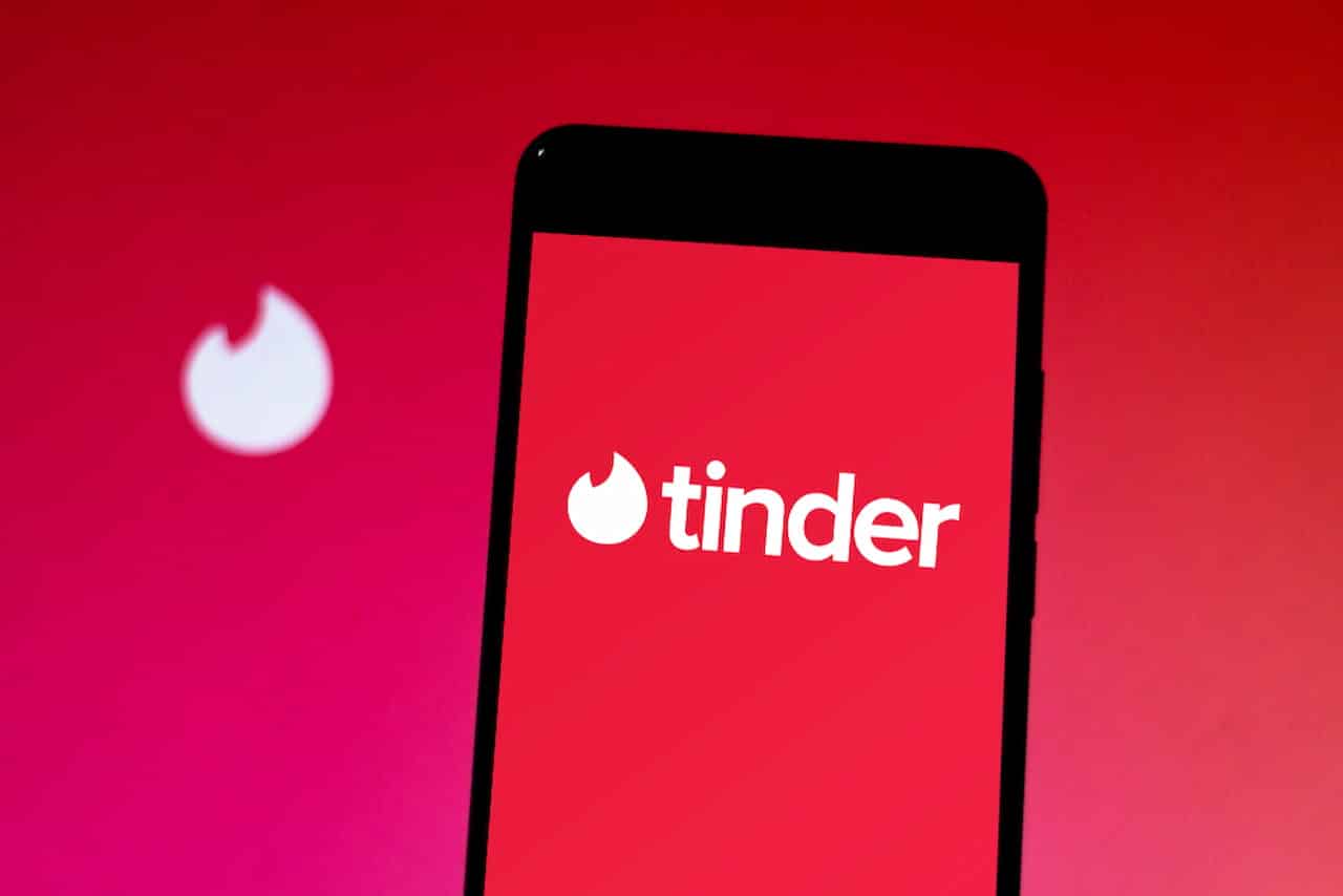 celular exibindo aplicativo com o logo do Tinder, há um fundo vermelho atrás do celular