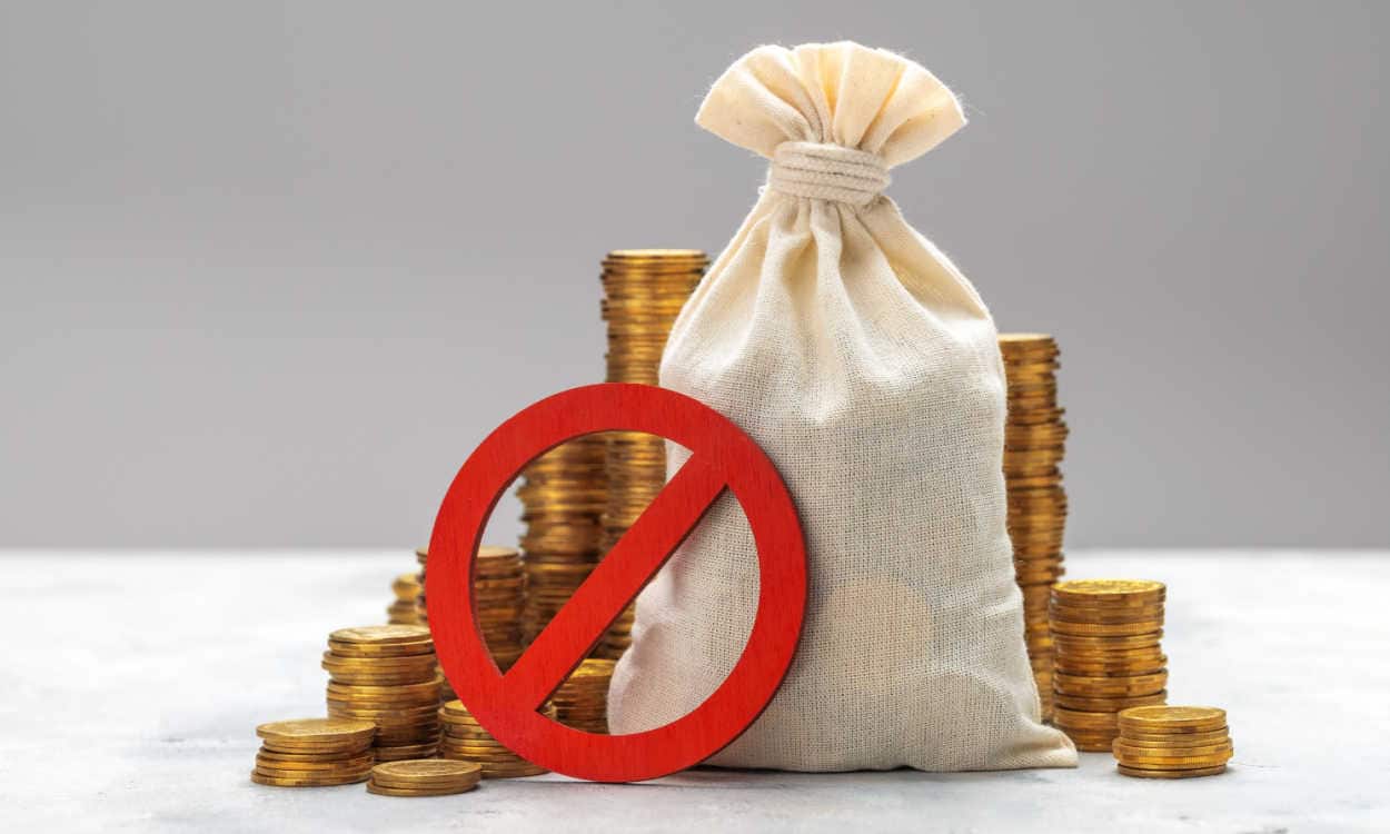 Saco de dinheiro e várias moedas de ouros com sinal de proibido na frente representando um calote ou não pagamento de dívida.