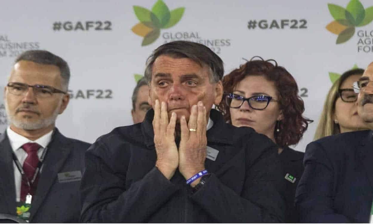 Jair Bolsonaro passando as mãos no rosto com cara de preocupado durante evento.