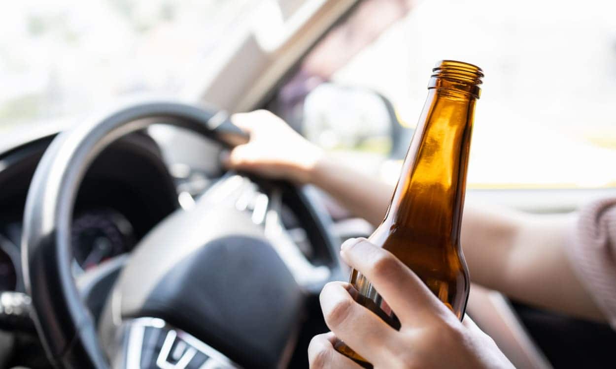 Pessoa com garrafa de bebida enquanto dirige álcool volante